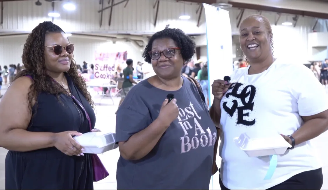 Three Dessert Wars fans holding takeout boxes inside the fairgrounds hall.