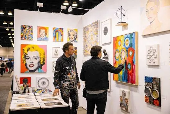 Two visitors looking at colorful paintings inside an artist booth at Art Fair Tampa