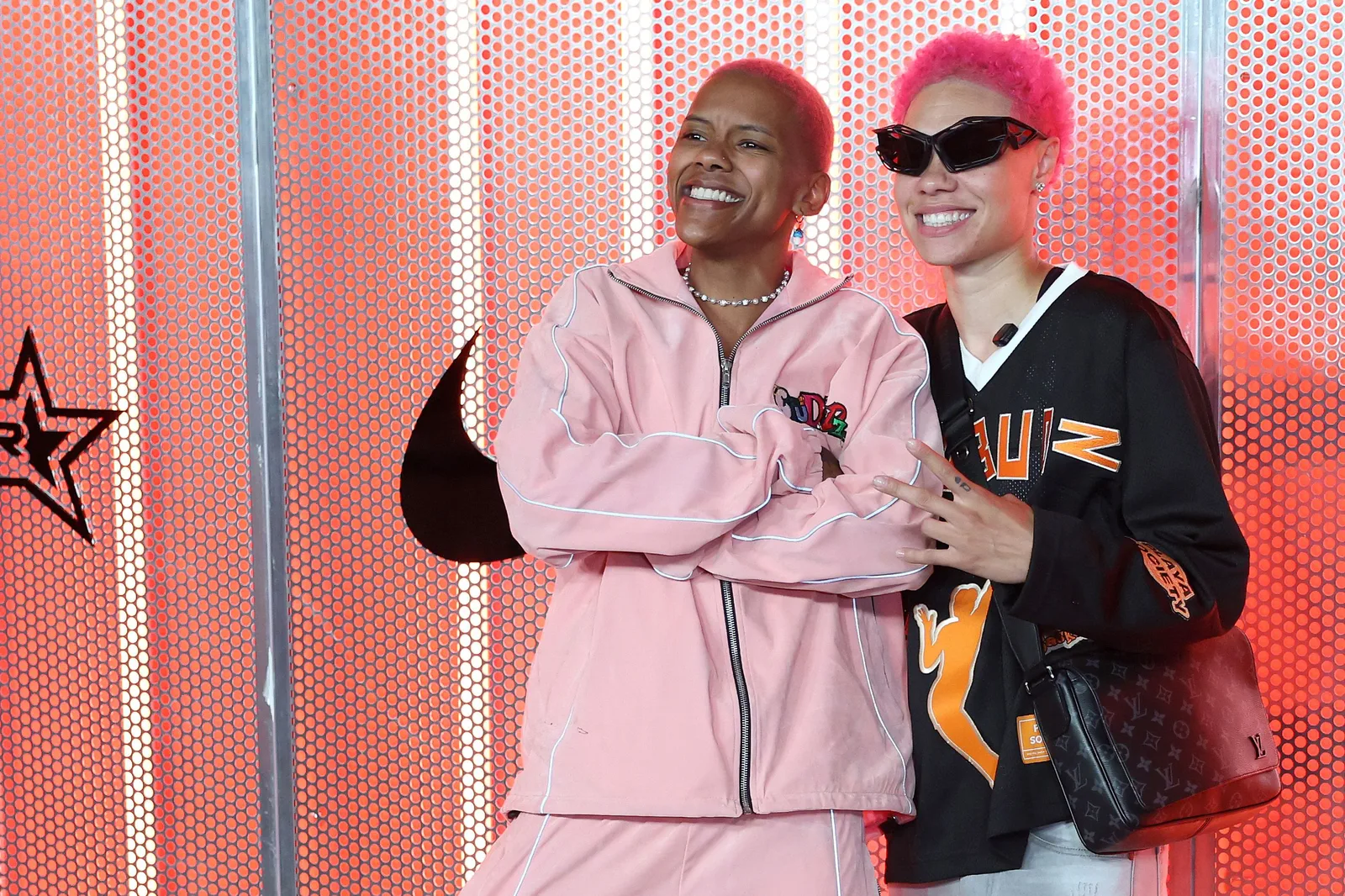 Minnesota Lynx players Natisha Hiedeman in a pink tracksuit and Courtney Williams in a black jersey and sunglasses, the StudBudz streamers, posing together against a red dotted wall