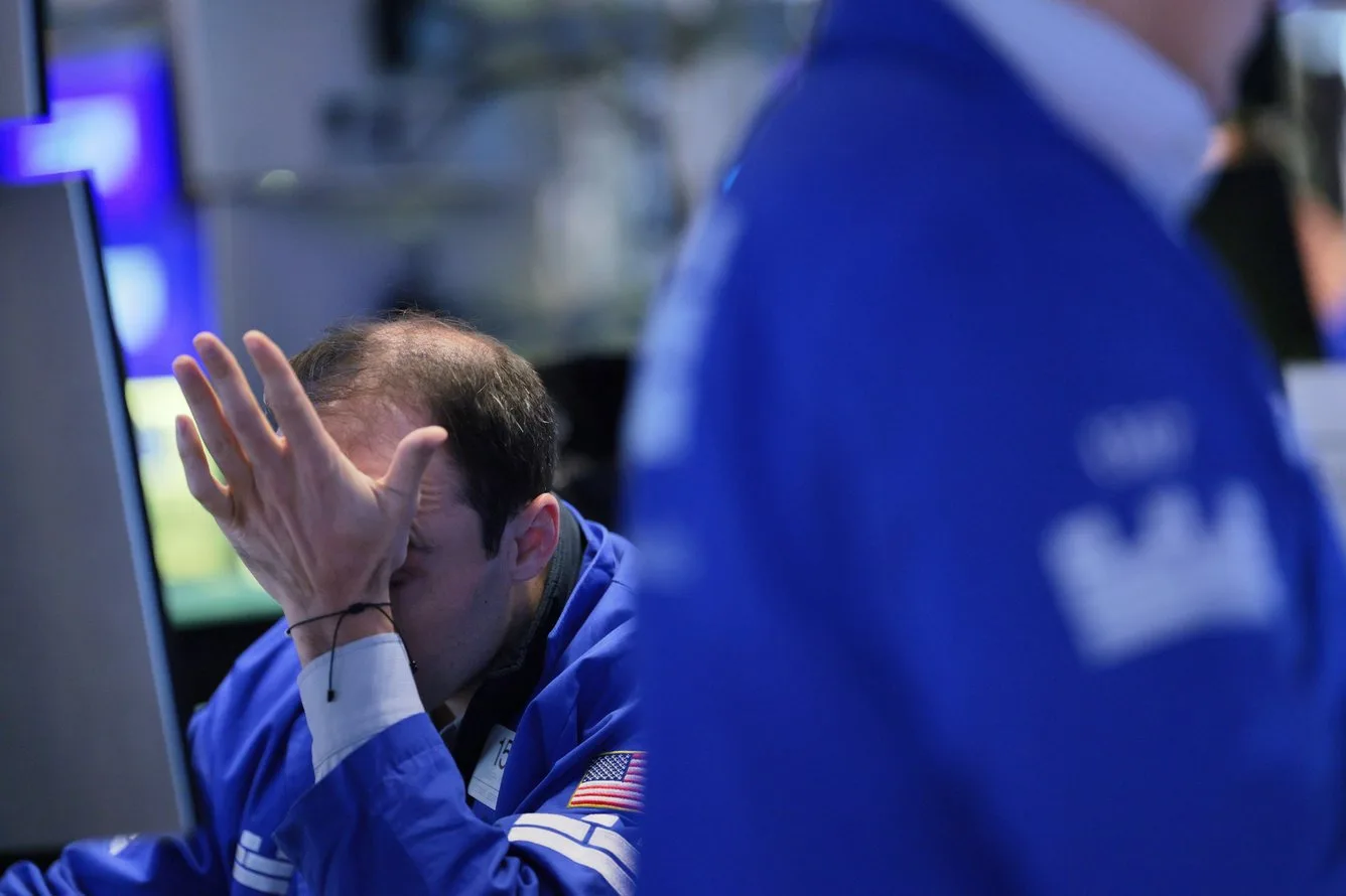 A trader in a blue jacket on the New York Stock Exchange floor holding his head in his hand during a market selloff