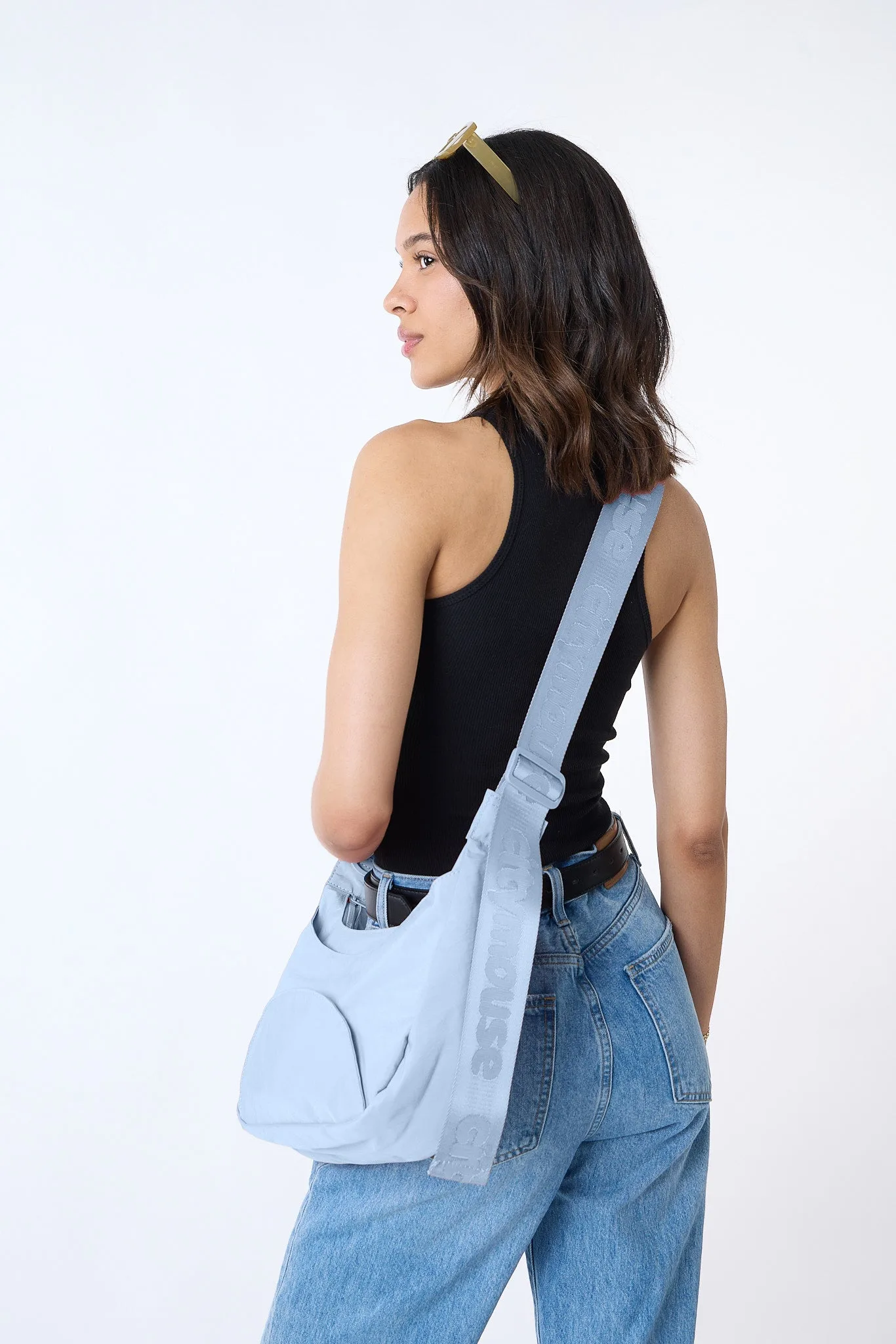 A model wearing the sky blue citymouse Park crossbody bag with a wide branded strap, photographed against a white background