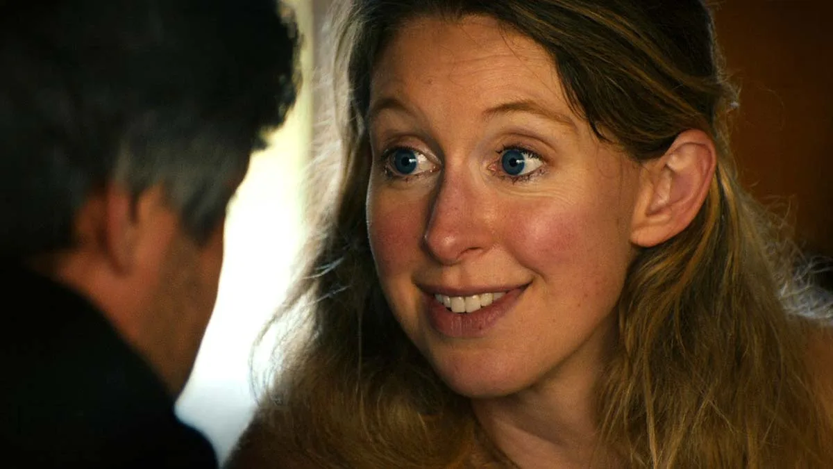 Elizabeth Holmes in close up, smiling as she speaks with Nathan Fielder, whose back is to the camera, in a still from You Can See Everything