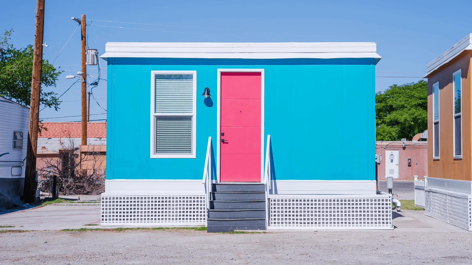A bright blue Boxabl Casita factory built home with a pink front door, installed on a lot