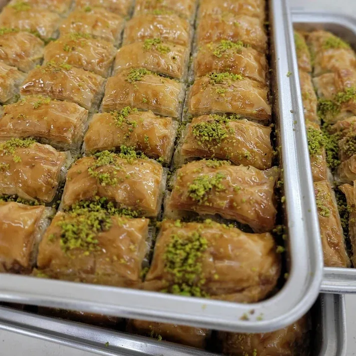 A metal tray of glossy pistachio topped baklava pieces from Good Baklava, cut in neat rows and sprinkled with ground green pistachio