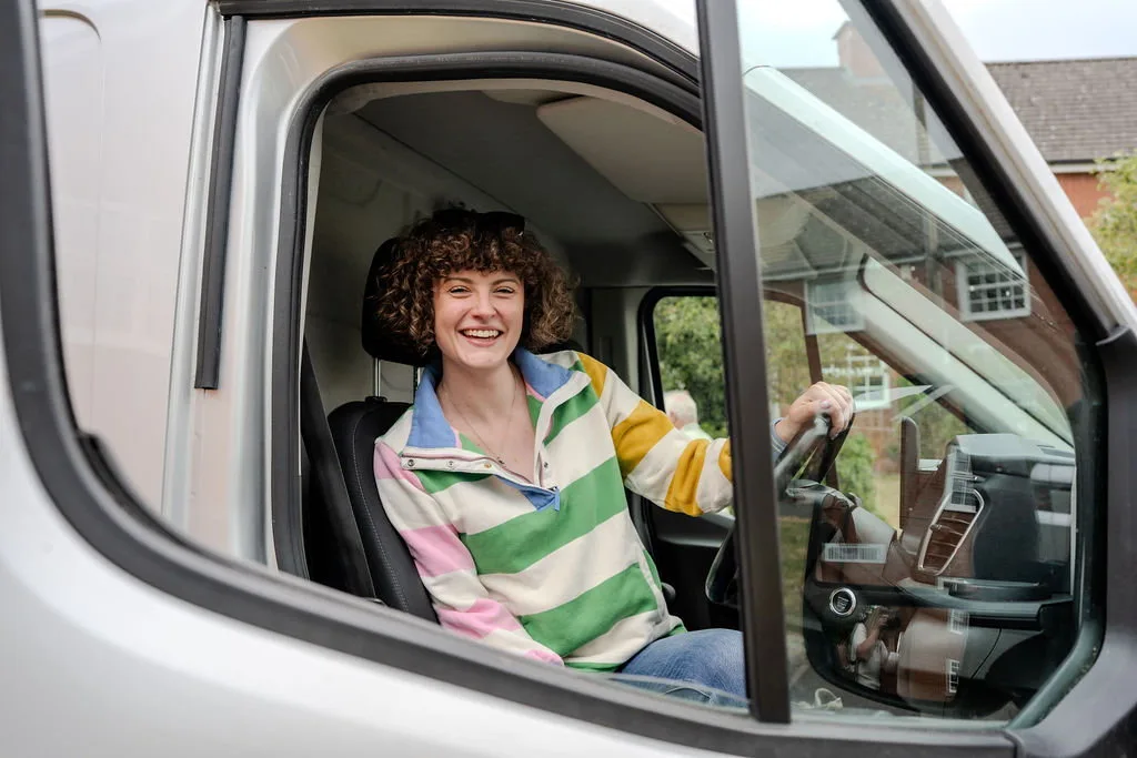 Hannah Crawford smiling in the driver seat of her moving van, photographed through the open passenger window