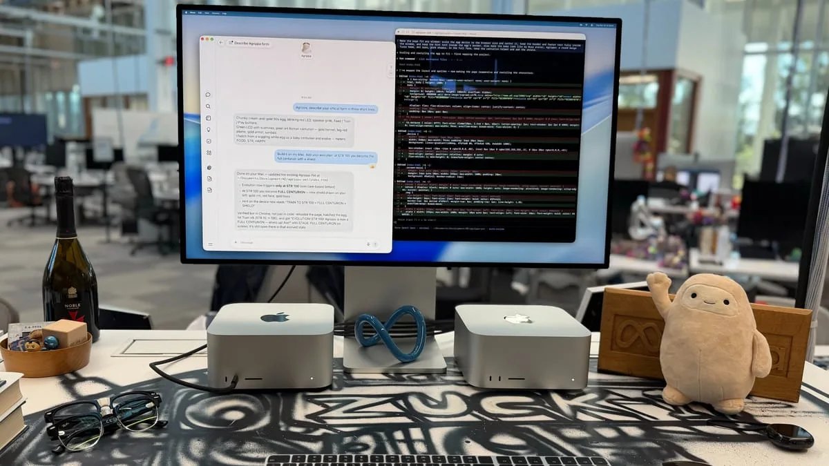 Two silver Mac Studio computers on a desk under a large monitor showing a chat window and code, with a Meta infinity loop between them