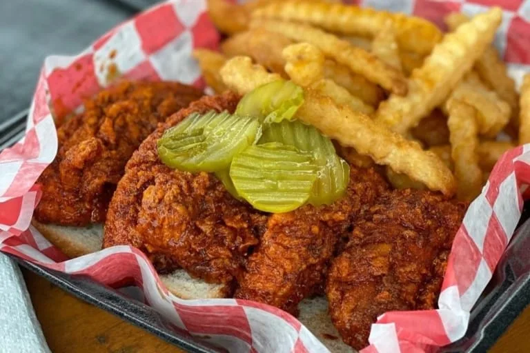 A plate of bright red Nashville hot chicken with pickles and white bread at Princes Hot Chicken