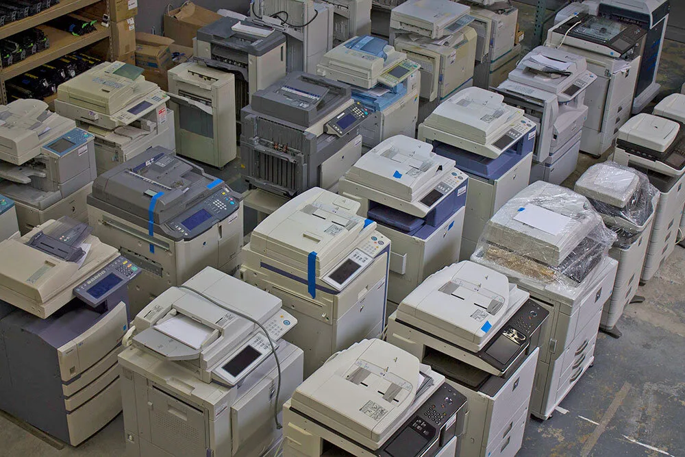 Rows of retired office copiers and printers waiting in a warehouse for resale or recycling