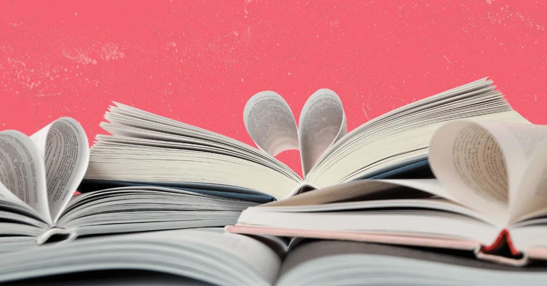 Open romance novels with their pages folded into heart shapes against a pink background