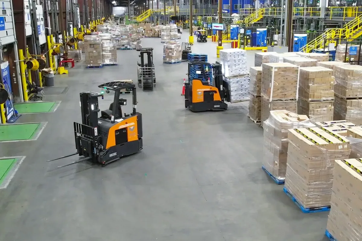 A warehouse floor with forklifts moving tall stacks of palletized goods