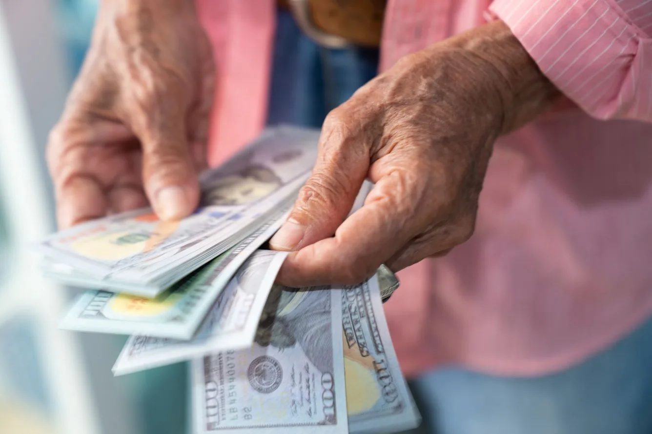 An older person hands counting a stack of one hundred dollar bills